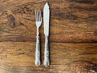 Pair of fish fork and fish cutter showing silverplate ornate handles, wood background.