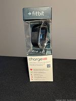 Brand new Fitbit Charge HR wristband in its original transparent plastic box with visible Fitbit logo on top and the product name and features on front.