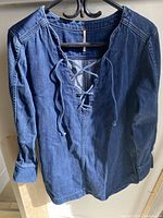 Front view of blue denim tunic by Free People. Shows lace-up detail at neckline and long sleeves.