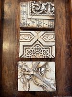 Three tiles stacked on wooden surface showing front reliefs