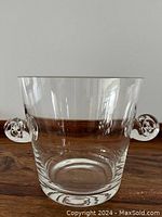 Front view of clear glass ice bucket with two curled handles, placed on wooden surface.