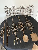 Set of four vintage wrought iron fireplace tools with intricate filigree detailing laid on a black surface along with the decorative hanging mount.