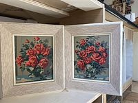 Two framed paint by numbers paintings of roses in vases side by side, placed on a shelf.