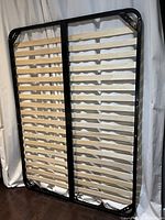 Full view of the bed lift system showing black metal frame with wooden slats horizontally aligned