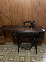 Front view showing the Singer sewing machine mounted on the wooden table with drawers and metal base including foot pedal.