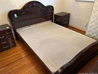 Brown/black lacquered wooden bed frame including headboard, footboard, side rails, and metal base, shown without mattress on wood floor between two matching nightstands.