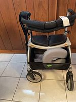 Front view of Evolution walker with seat and basket containing canes, showing front wheels and padded seat.