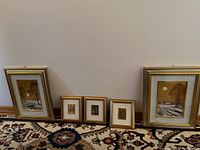 Wide shot of all five framed prints displayed on floor against wall, showing two large prints and three smaller prints