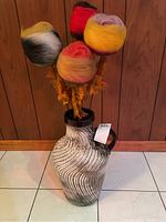 Photo showing entire large ceramic vase with black and white swirl design and six multicolored handmade felted flowers inside.
