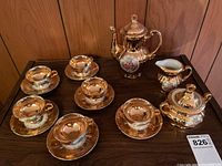 Full set showing 6 demitasse tea cups with saucers, creamer, sugar bowl with lid, and small teapot, all gold-tone with painted details.