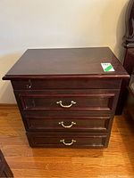Front view of first lacquered brown-black night stand showing three drawers with brass handles