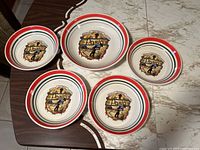 Top view of one large serving pasta bowl centered with four smaller matching bowls arranged around it showing the pasta-themed illustration and rim colors.