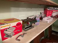 Ampia Brevettata pasta maker with shiny chrome finish next to original box and detachable handle clamp on a countertop.