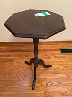 Front left view of octagonal wood pedestal stand showing turned central column and tripod base on hardwood floor.