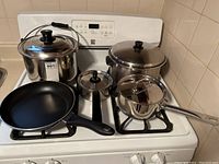 Five-piece set on stove including two large pots with lids, a small saucepan, a saucepan with lid, and a non-stick frying pan.