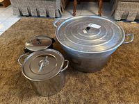 Set of three aluminum pots of varying sizes, arranged on carpet with furniture background.