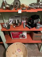 Shelf overview showing cast aluminum press housing, stainless steel bowl, plastic chute, instruction manual, motor unit, and packaging boxes