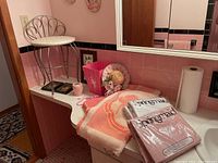Overview of vanity top with pink bathroom accessories, towels, and sealed sheet sets.