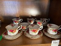 Set of six tea cups with saucers displayed on a wooden shelf showing floral pattern and gold trim