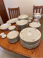 Full view of the china set arranged on a wood table showing plates, bowls, teapot, terrine, gravy boat, platters, and cups.