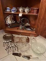 Photo of vintage servingware displayed in cabinet with cups, platters, and utensils.