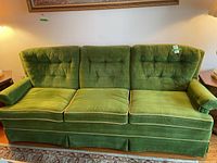 Front view of vintage green velvet three-seater couch by Sklar with mustard yellow piping and button tufting on cushions and back. Couch is high-backed and has skirted bottom.