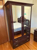 Front view of the brown-black lacquered wardrobe with two mirrored doors and two drawers.