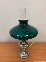 Full view of the Aladdin brass #11 hurricane table lamp with green glass shade and glass chimney, showing condition and overall appearance.