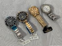 Four wristwatches displayed: two TEVISE automatic watches with black dials and stainless steel bands, two REGINALD quartz watches with crystal bezels, gold and silver tone metal bracelets.