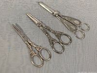 Three vintage silver plated grape cutting shears laid next to each other showing general design and condition.