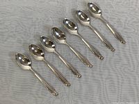 Eight sterling silver espresso spoons arranged in a row on a white patterned cloth.