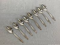 Eight sterling silver coffee spoons lined up on fabric, showing full length and design.
