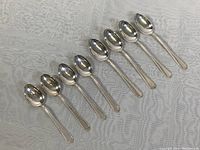 Eight sterling silver spoons arranged in a row on white cloth