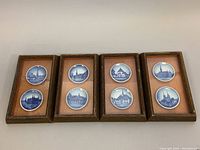 Four wooden frames each with two small blue and white Royal Copenhagen plates depicting Danish scenes arranged on white surface