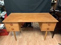 Front view of wooden desk showing rectangular top, tapering round legs, and drawer banks with wooden knobs and keyhole
