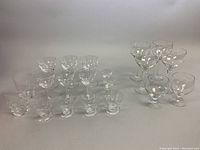 Overview of multiple crystal stemware glasses varying in size and style, arranged in groups on flat surface.