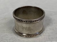 Front view of monogrammed sterling silver napkin ring showing engraved script initials MGB with beaded edges.