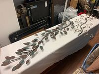 Full view of the iron metal leaf wall art showing the elongated branch with multiple leaves and crystal drop section.