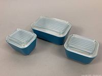 Three vintage Pyrex refrigerator dishes with clear ribbed lids, arranged to show size differences and condition.