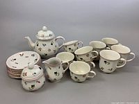 Full view of porcelain tea set including plates, teapot, creamer, sugar bowl, mugs, cups, and saucers with floral motif.