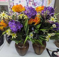 Two brown ceramic vases with colorful faux flower bouquets arranged on a table.