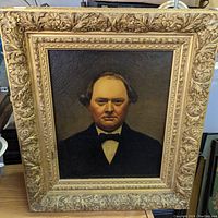 Front view of antique oil painting depicting a stern man in formal wear with detailed ornate floral carved frame.