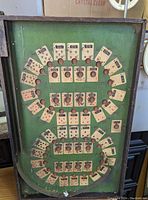 Top view of green wooden game board featuring poker card illustrations arranged in two circular patterns with metal pins inserted at card points.