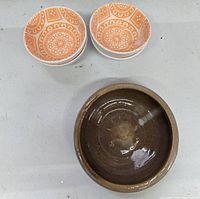 Top view of four small decorative orange and white ceramic snack bowls stacked and one brown pottery bowl.