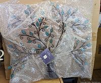Photo of metal ornament display stand wrapped in bubble wrap showing tree branch and teal leaf design.