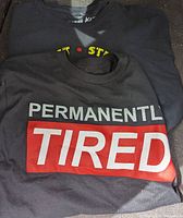 Photo of black T-shirt with 'PERMANENTLY TIRED' text printed on the front