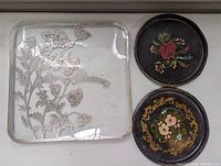 Square glass tray showing etched floral design and '25th Anniversary' banner with two round floral painted trays beside it.