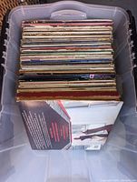Top view of one large plastic bin filled with vinyl record albums arranged upright showing spine edges and some cover art.