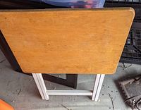Top view of a wooden TV tray with light brown rectangular surface and folding white legs, showing surface wear.