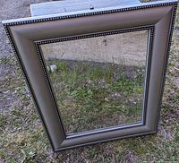 Square silver framed mirror resting outdoors with a decorative beaded border detail along the inner edge of the frame.